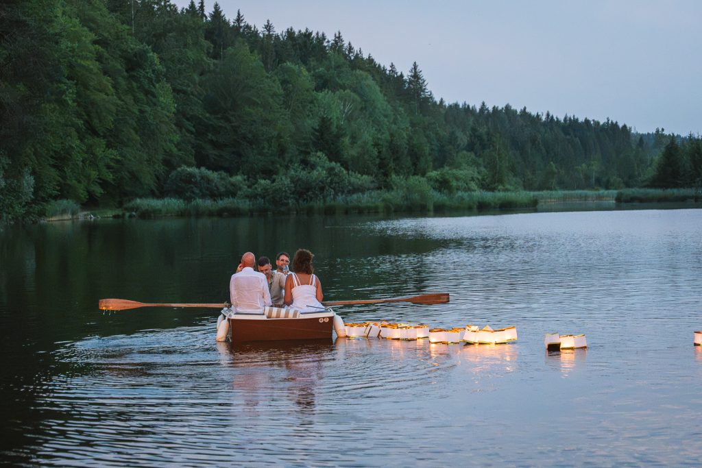 Menschen in einem mit Lichterketten geschmückten Boot auf dem Weiher. Abendstimmung.