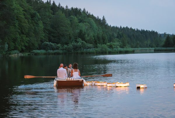 Menschen in einem mit Lichterketten geschmückten Boot auf dem Weiher. Abendstimmung.